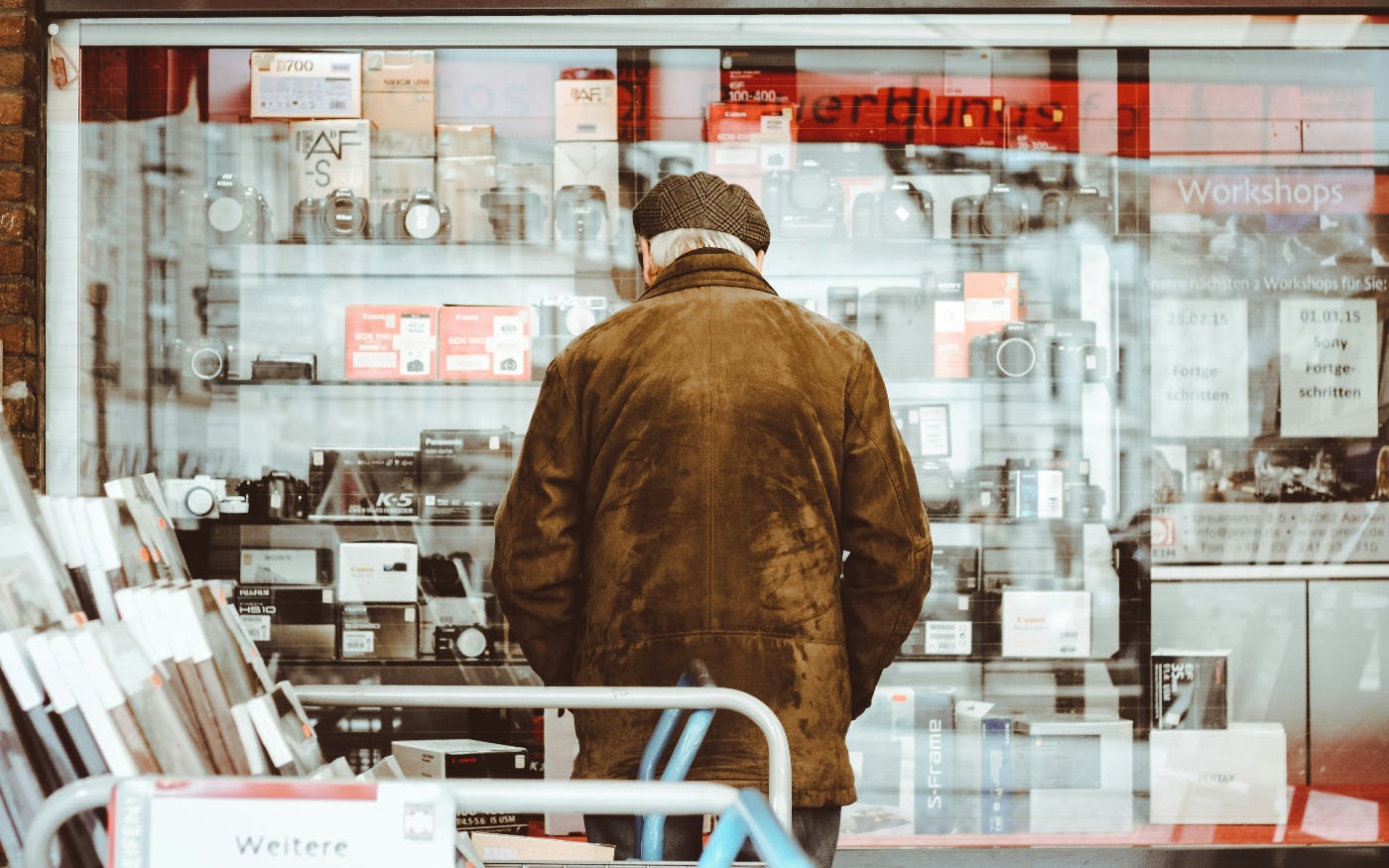 An older gent in a brown coat looking at cameras in a glass display case