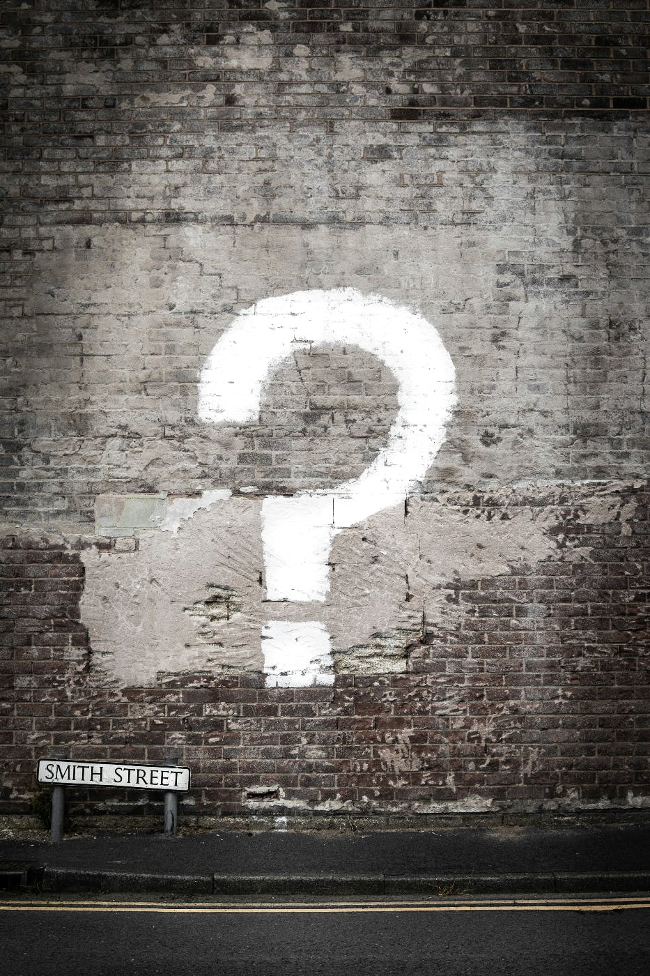 A plastered brick wall with a street sign in the lower left corner reading Smith Street and a large question mark painted on the wall