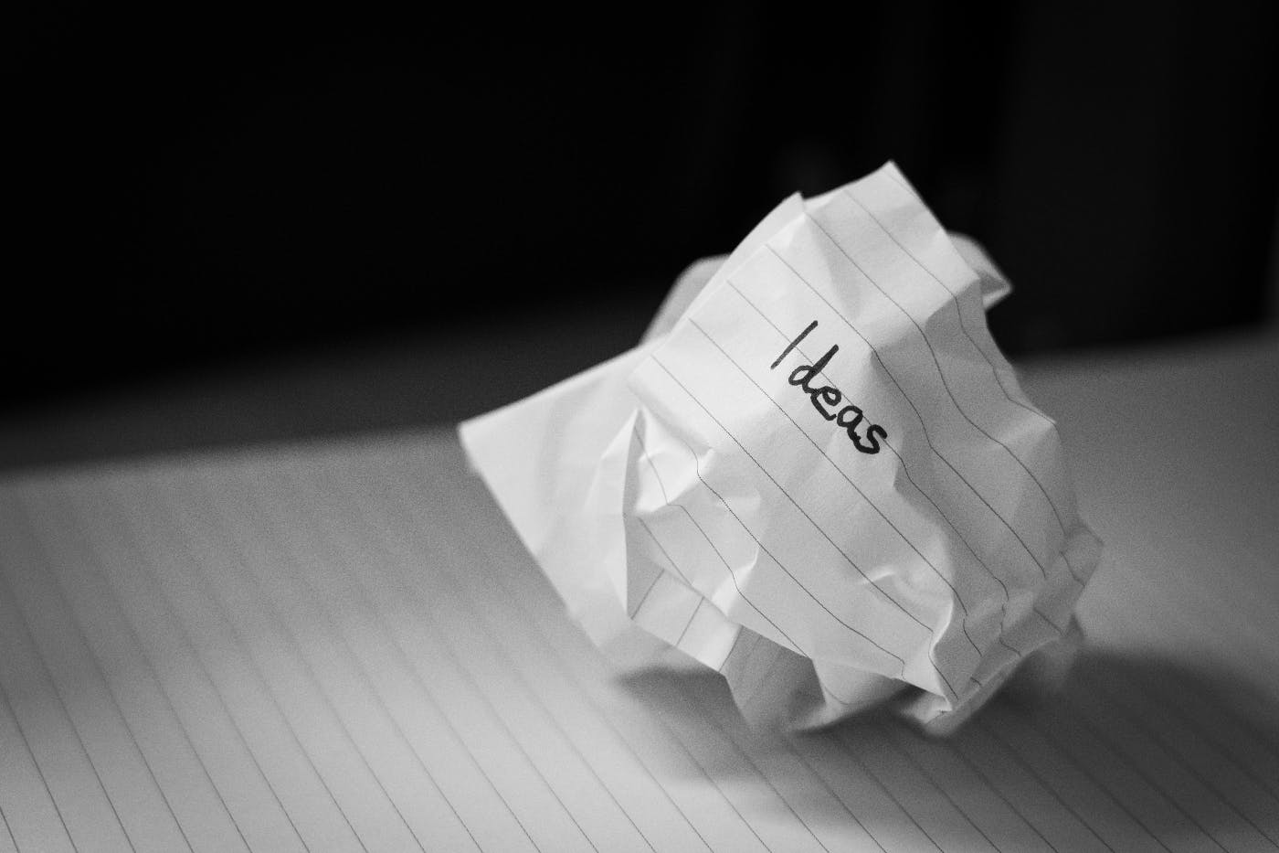 a black and white image of a crumpled piece of lined paper with the word ideas on it, sitting on a pad of lined paper