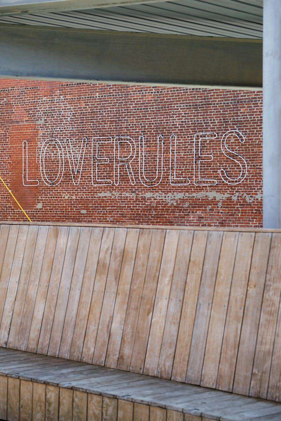 A brick wall behind a wooden bench with LOVERULES written on the wall