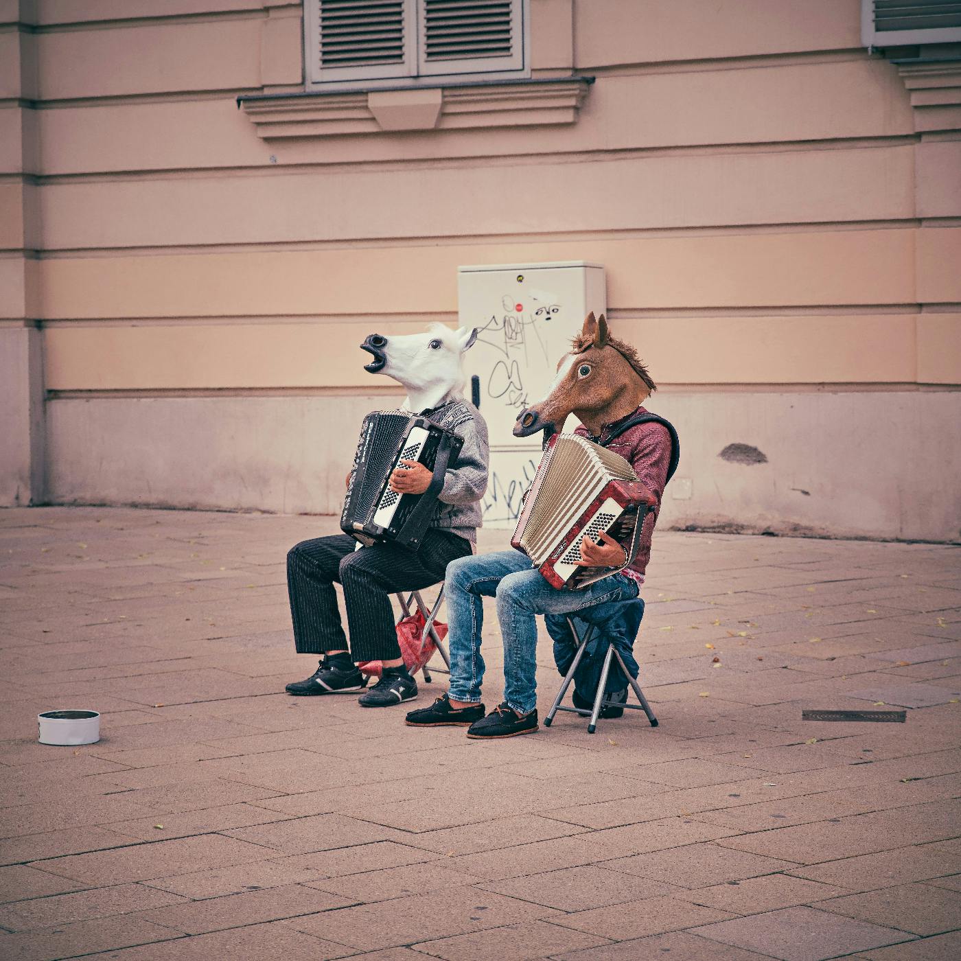 Two guys in horse masks, playing accordions, sitting out on the sidewalk
