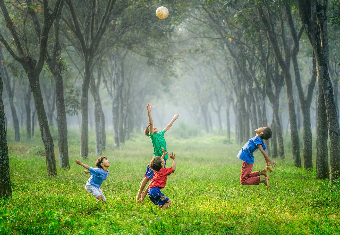 4 kids in a clearing throwing a soccer ball in the air