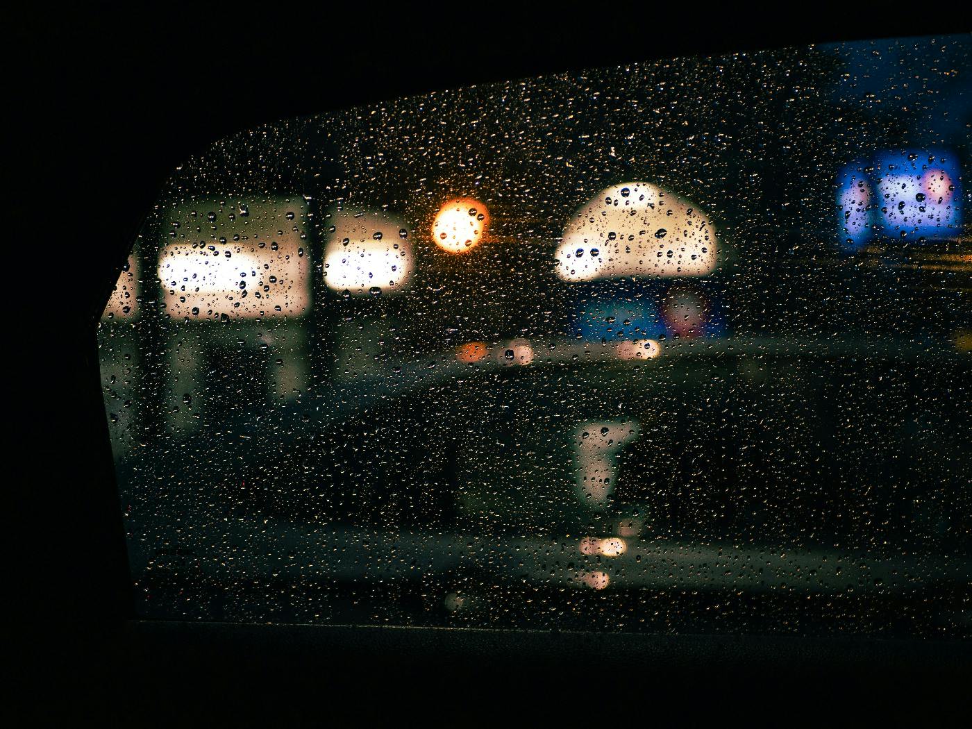 Shop lights through a rain spattered car window
