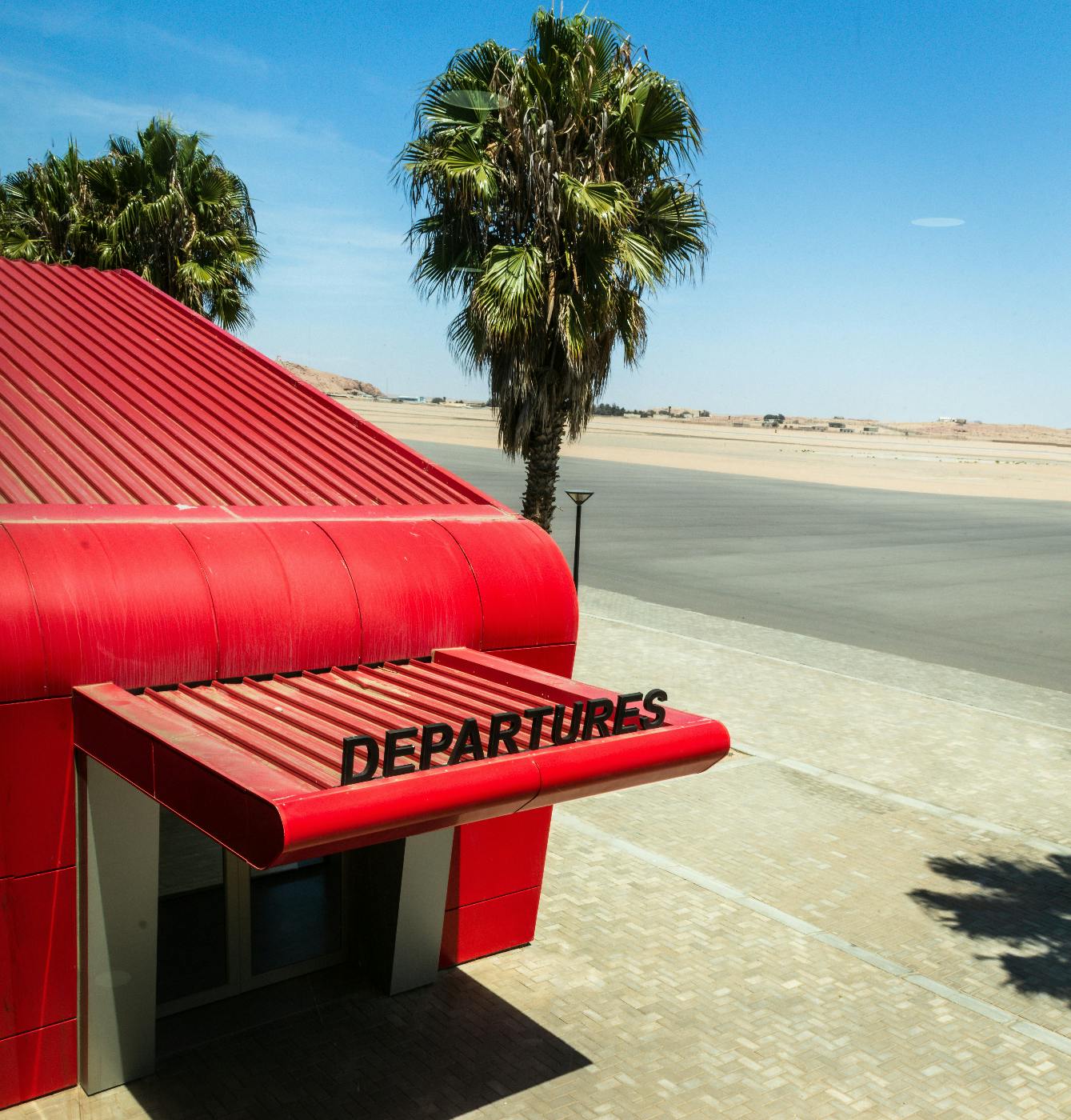 A red building by a palm tree with Departures written on the awning