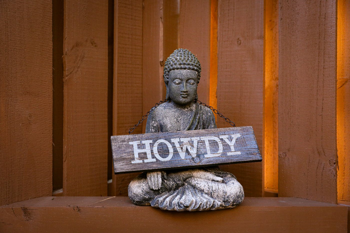 A seated Buddha statue with a wood sign hanging on it reading "Howdy"