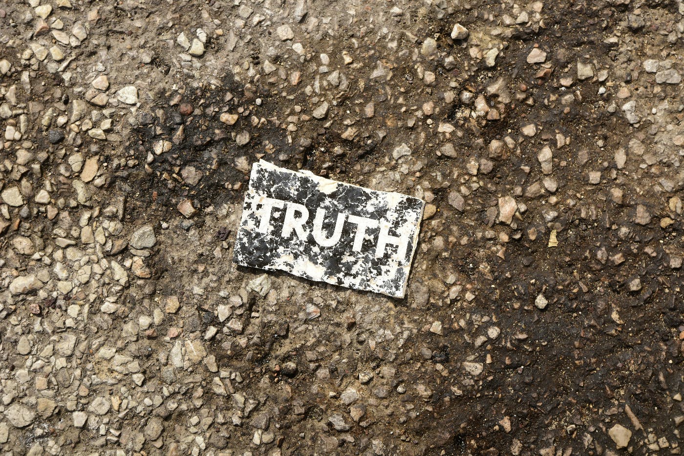 a battered metal sign reading TRUTH on a stone and dirt road