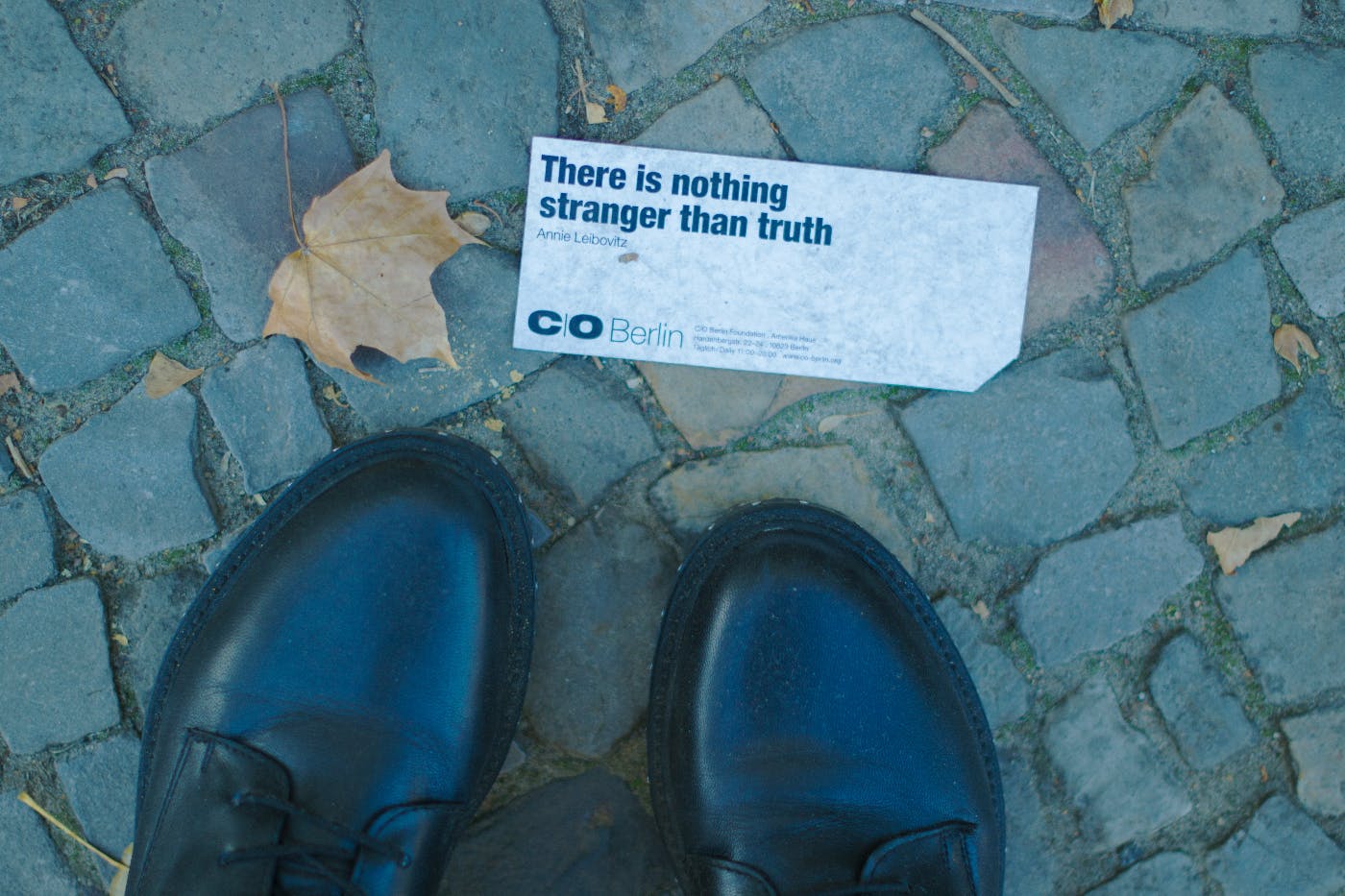 a view from above, a pair of black shoes and a slip of paper with There is nothing stranger than truth printed on it