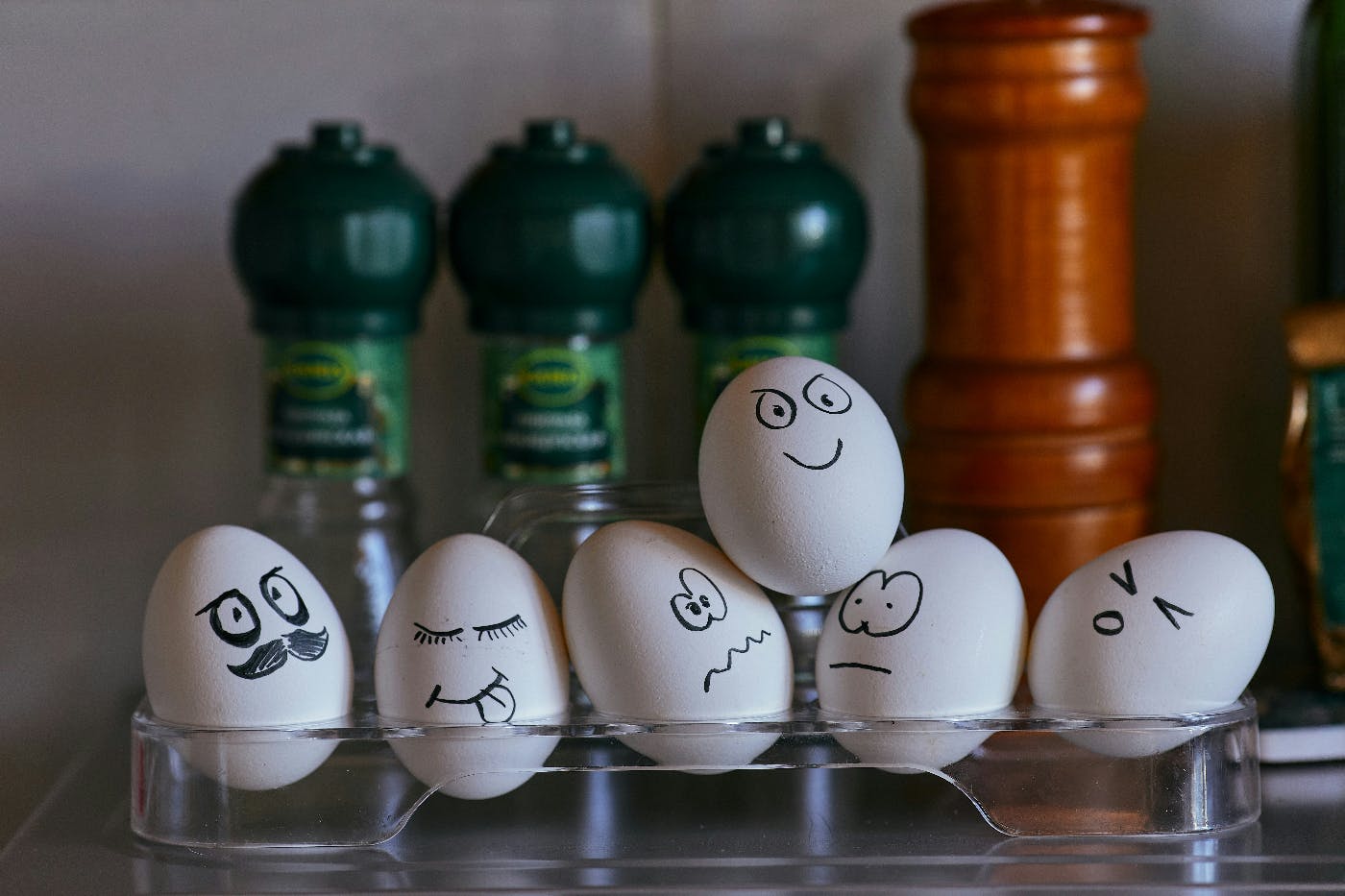 White eggs with faces drawn on with a sharpie in a cradle