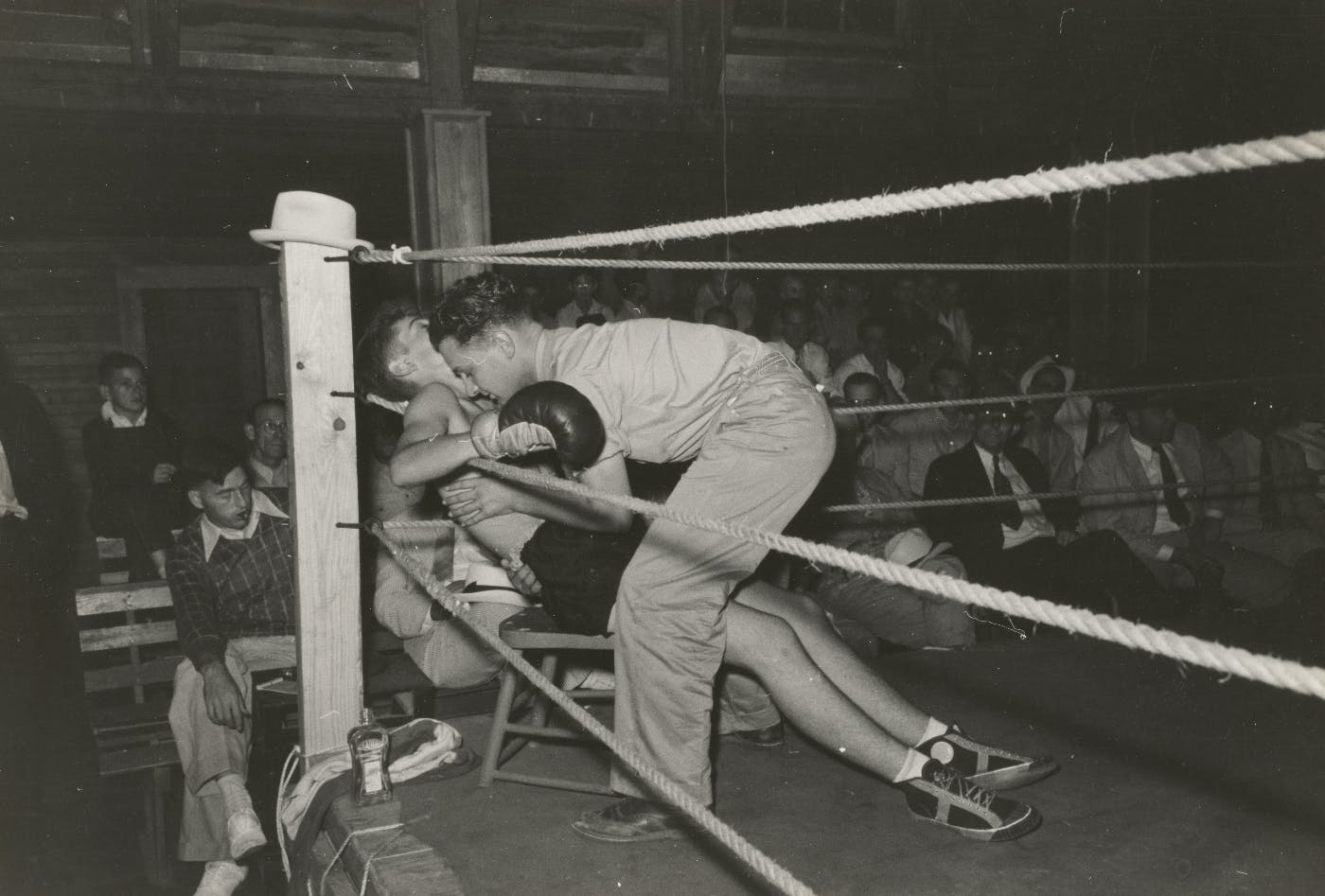 Black & white picture of a knocked out boxer being settled into a chair in his corner of the ring