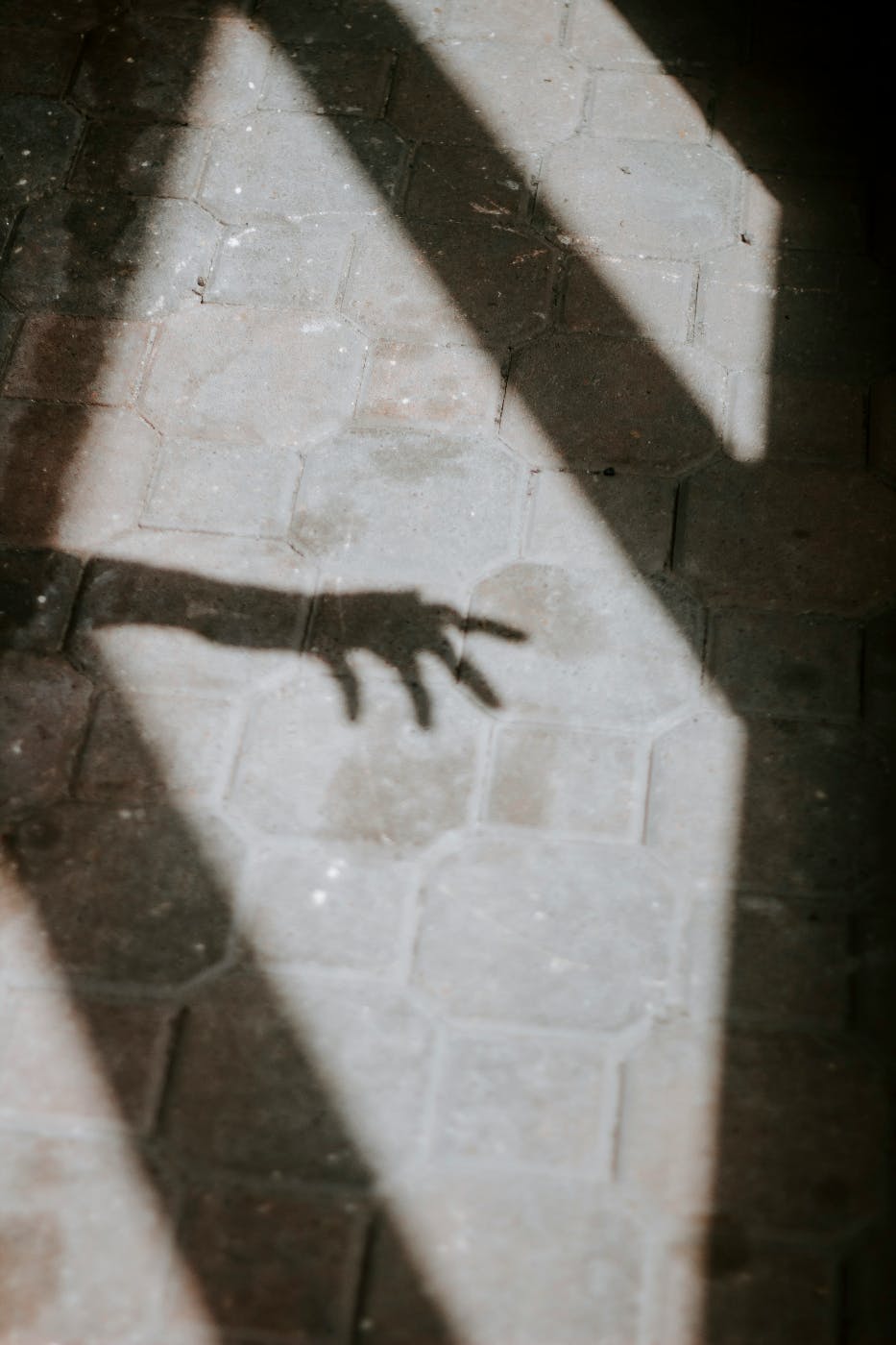 A shadow of a hand in window frames on a stone walkway