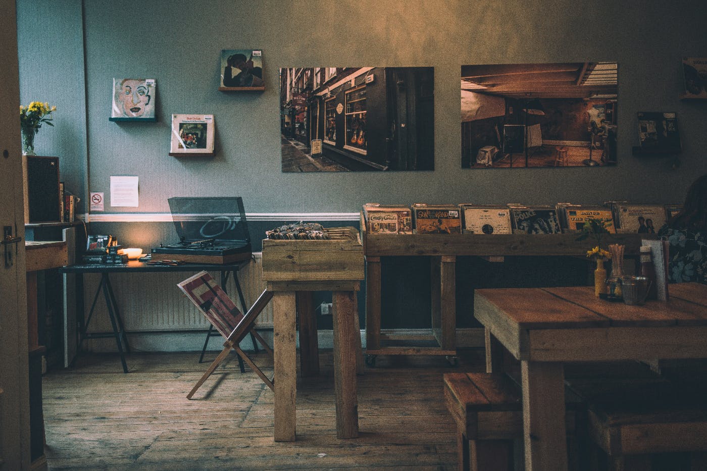 A dimly lit record shop with wood cases for records and wood tables for socializing