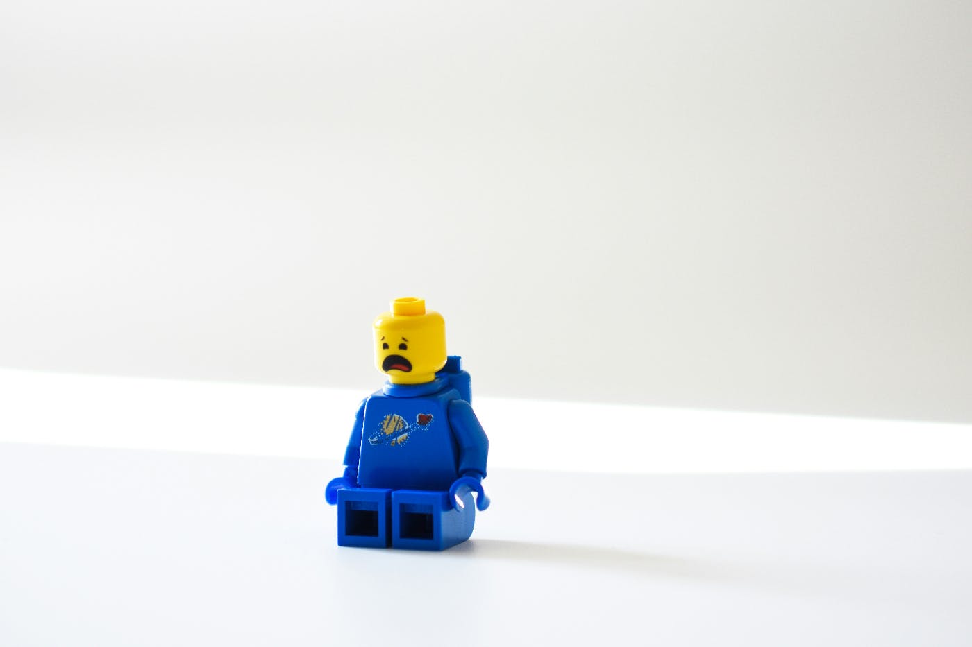 A little Lego man in blue sitting on a white floor weeping