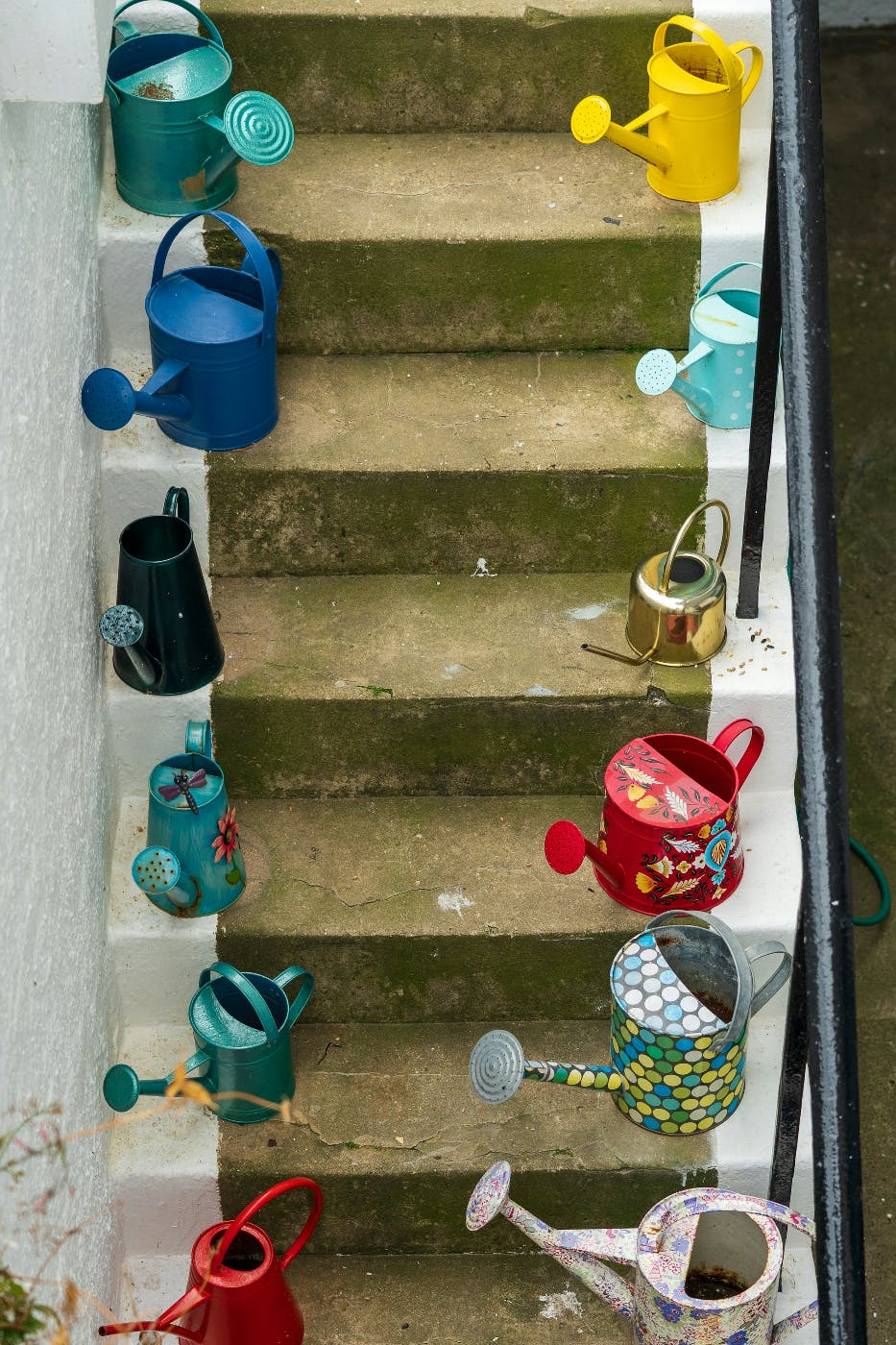 A narrow set of stairs with different size and style watering cans lining each side