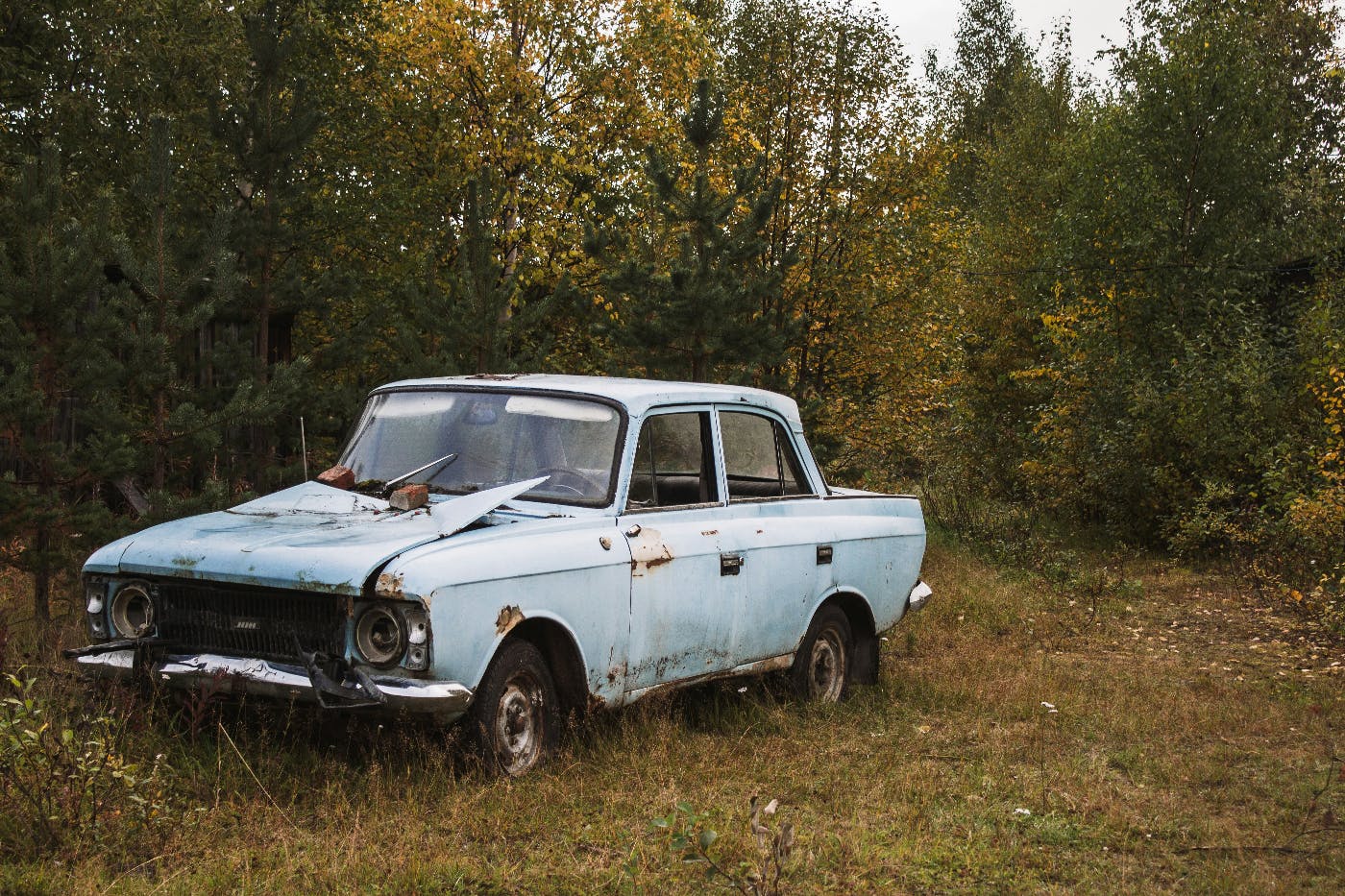 A beat up and rusted old blue car abandoned in a field