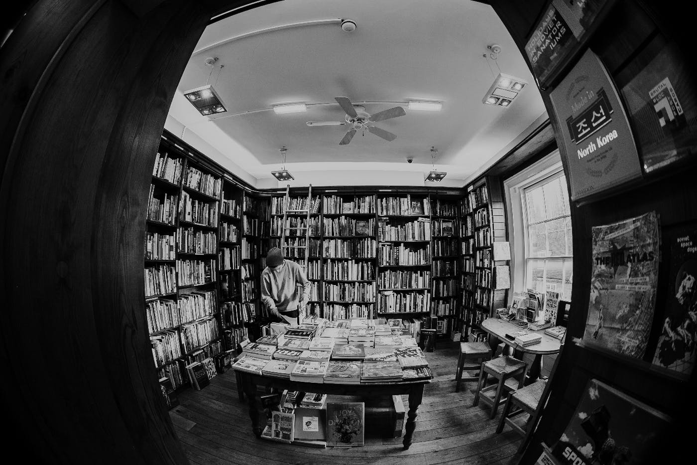 A black and white fisheye lens view of the inside of a bookstore with a young man browsing