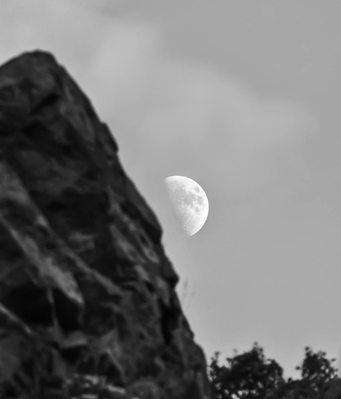 Grey scale photo of the moon in the background of a mountain