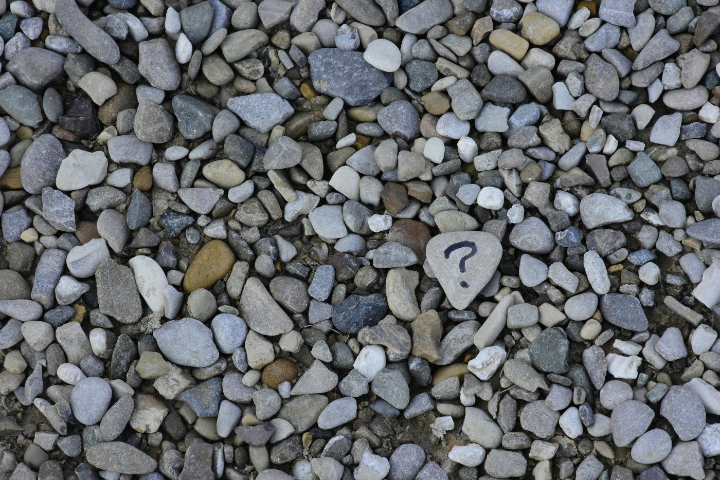 A mass of stones on a beach with one flat stone having a question mark written on it.