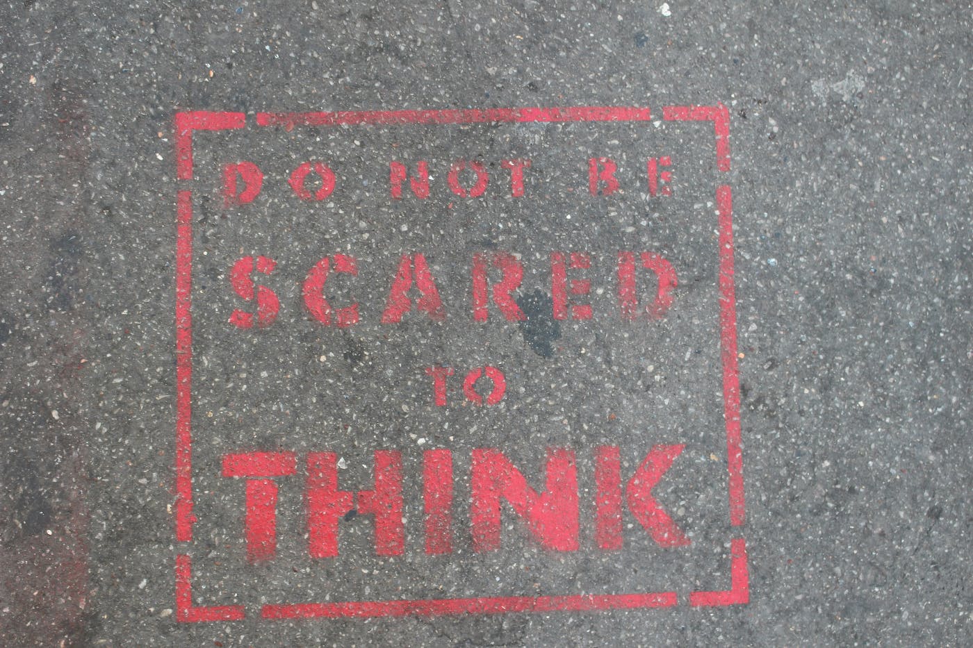 Red Stenciled words on pavement reading Do Not Be Scared To Think