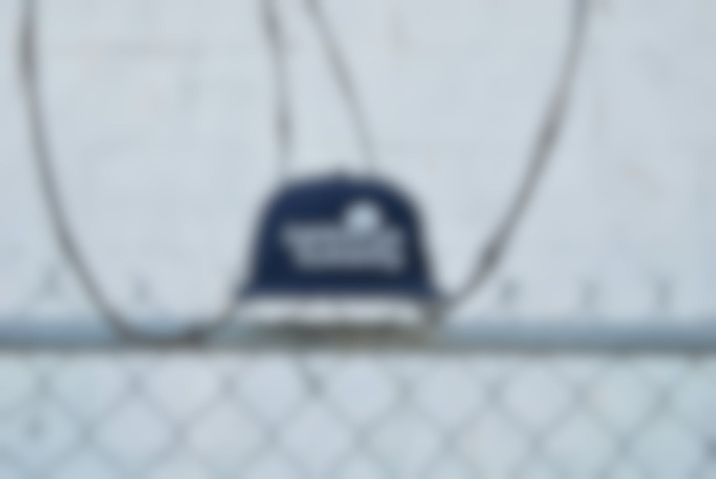 A blue baseball cap with Harmonize Humanity on it sitting on top of a fence covered with razor wire