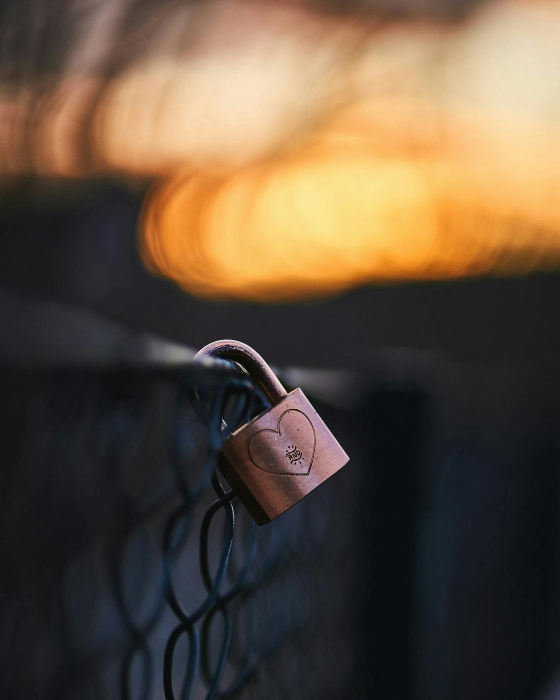 A padlock with a heart etched on it, locked on a fence