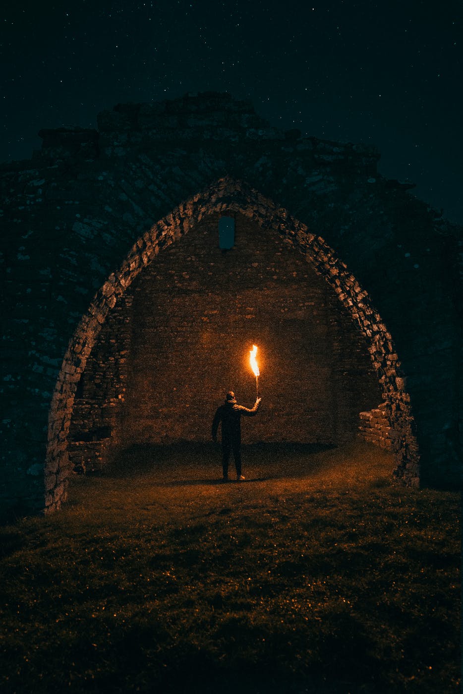 A man holding a torch under a stone arch