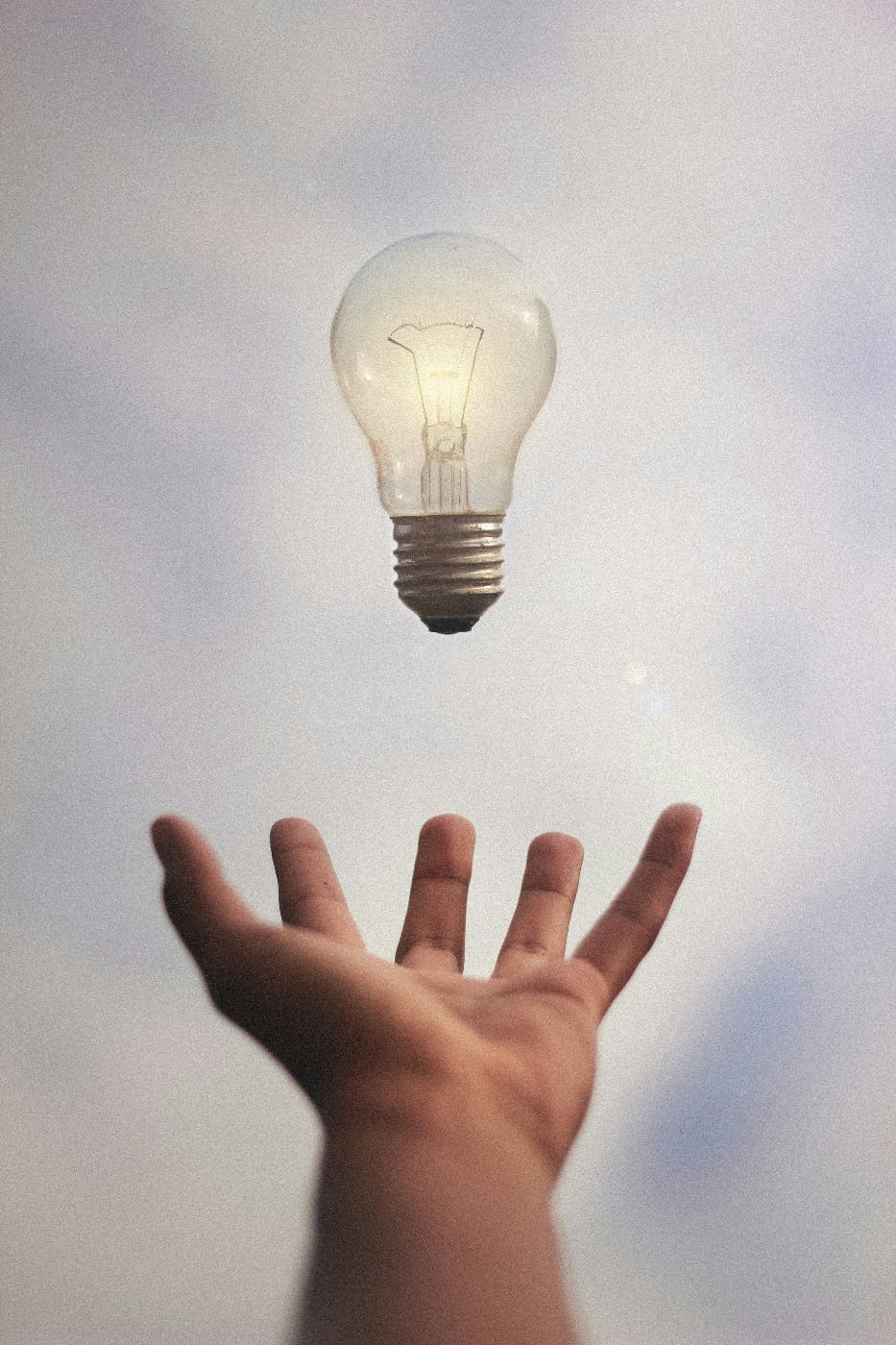 A lit light bulb floating over and outstretched open hand