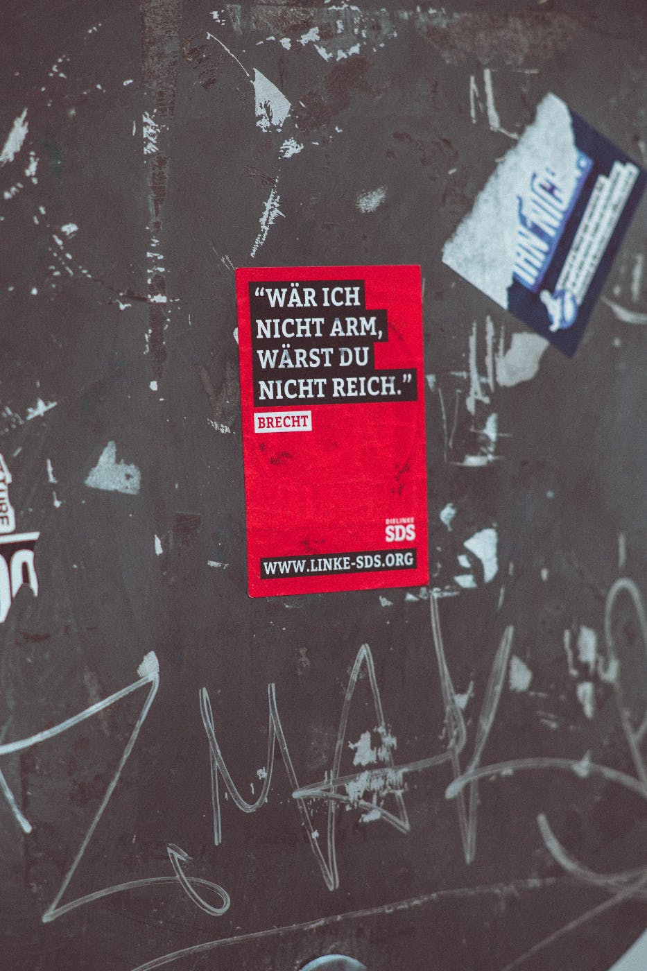 A grey wall with a red sign reading: war ich nicht arm wärst du nicht reich- Brecht