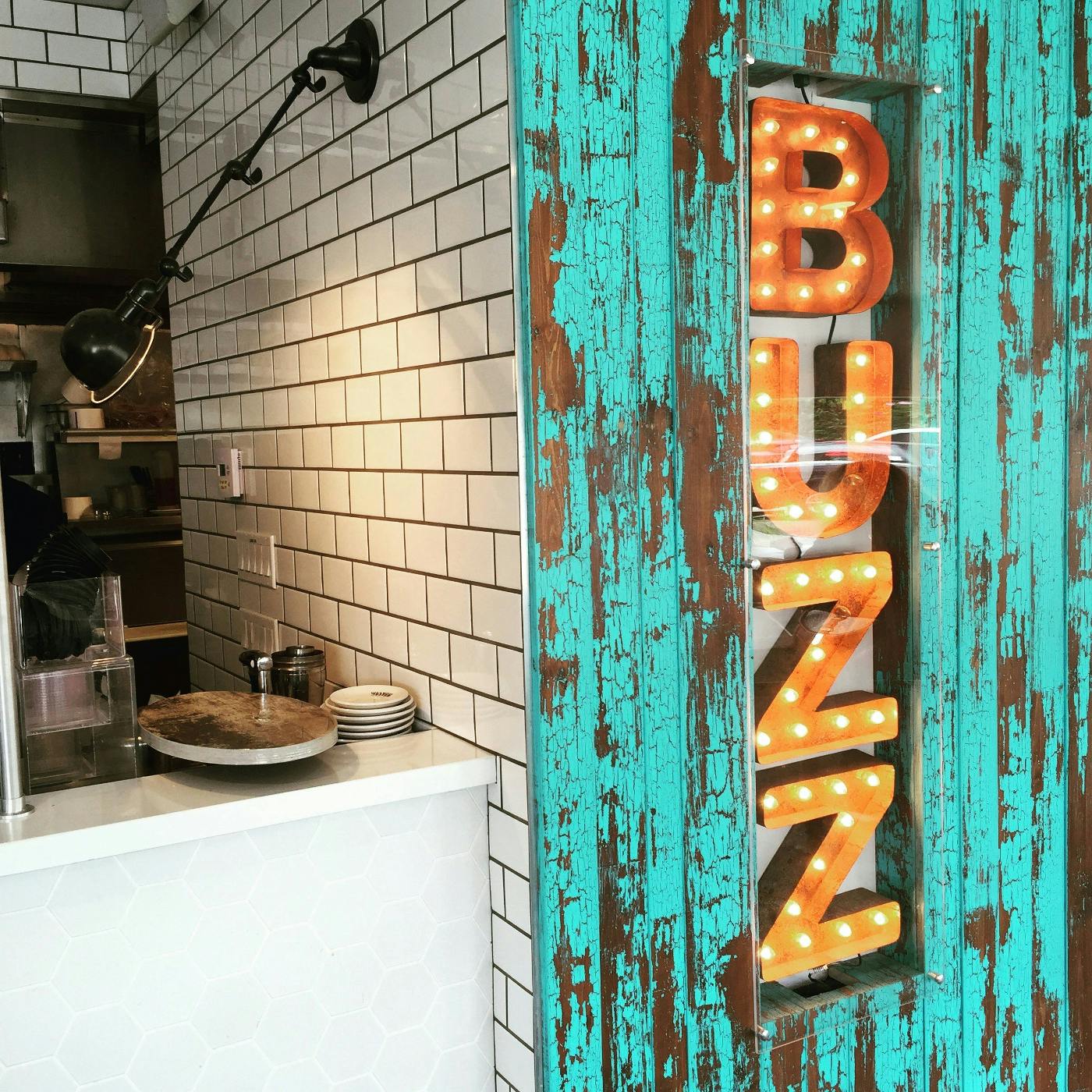 Interior of a coffee shop, the word buzz on the right  in big orange neon letters