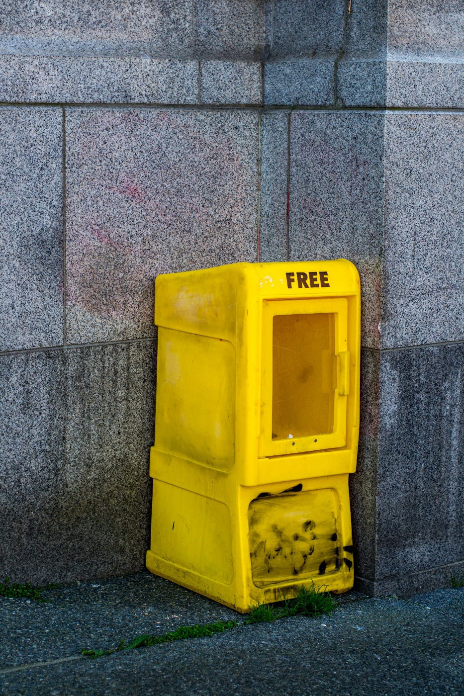 A dirty yellow newspaper rack with FREE printed on it, empty