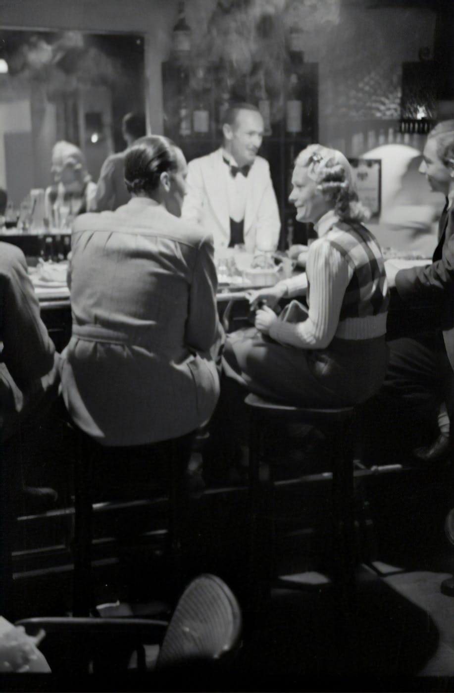 A grayscale image of a couple sitting at a bar circa 1940