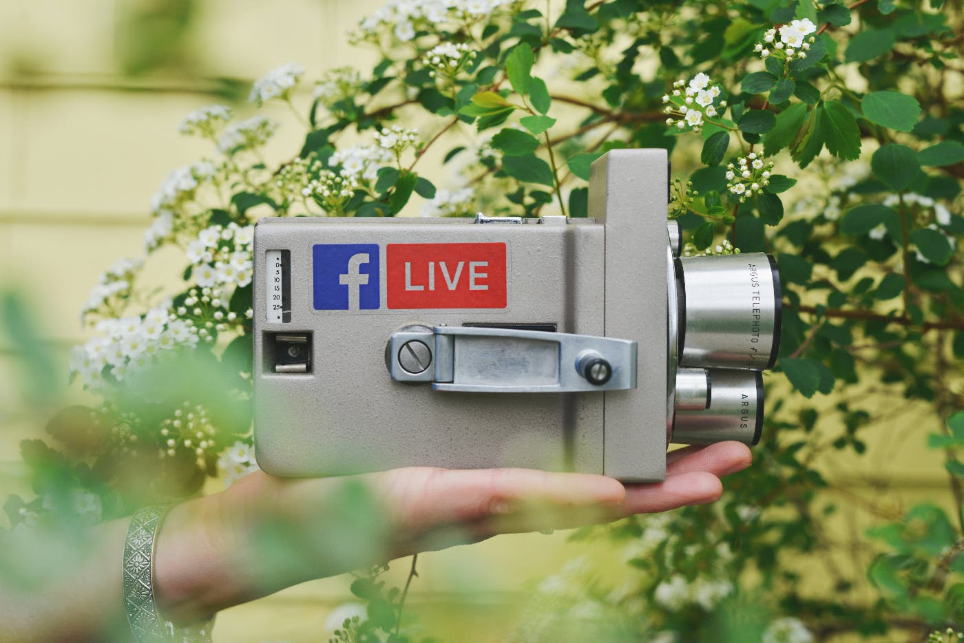 A hand holding a super 8 camera with the Facebook logo and Live n the side