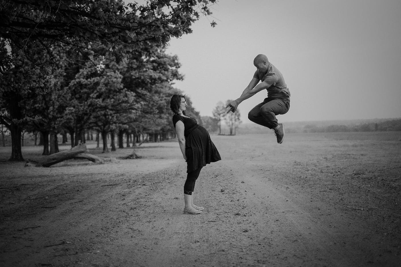 A pregnant woman and a man leaping in the air pointing at her stomach.