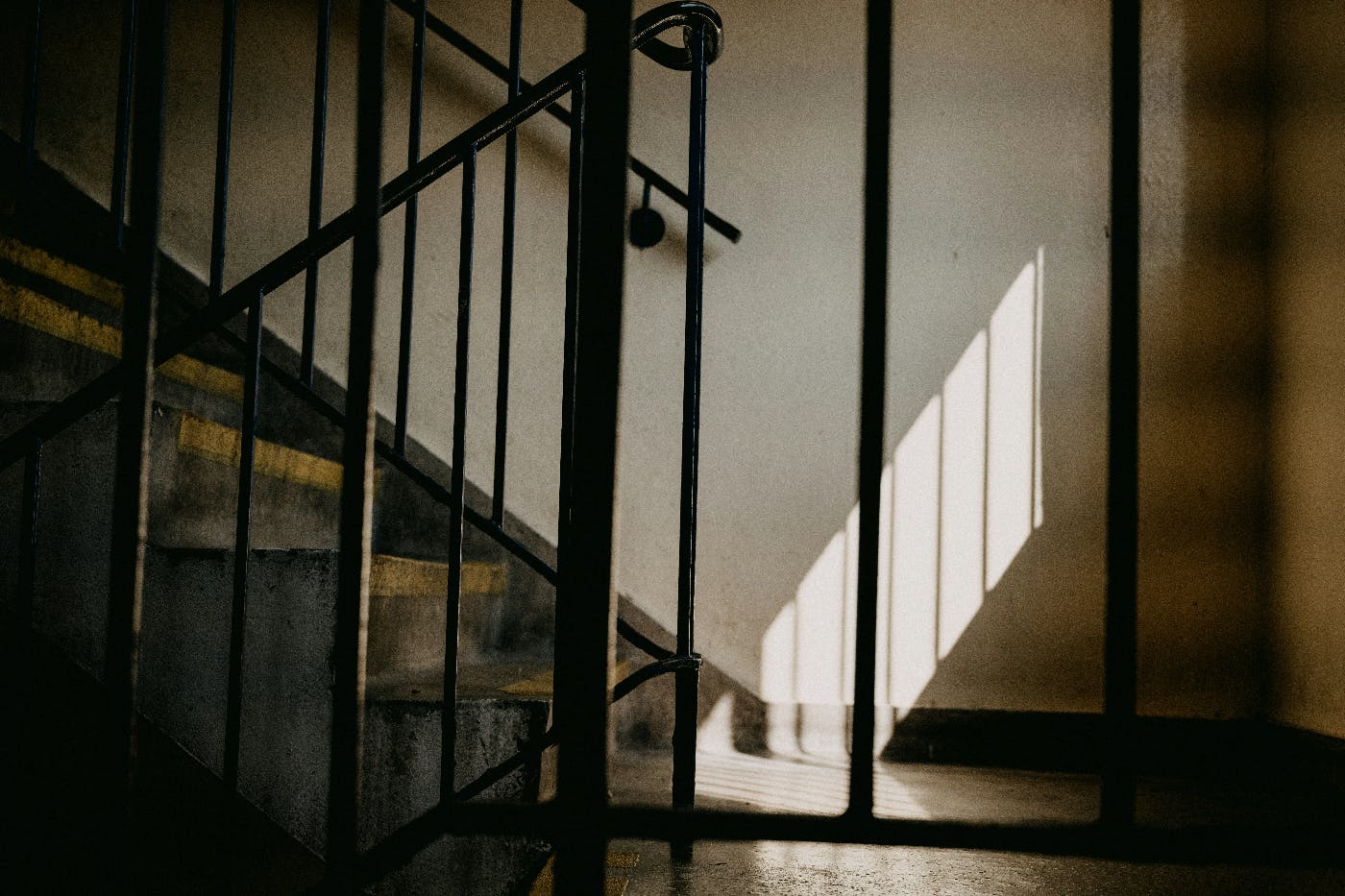 A staircase with black metal railings, wood flooring and sunlight coming through an unseen window on the right