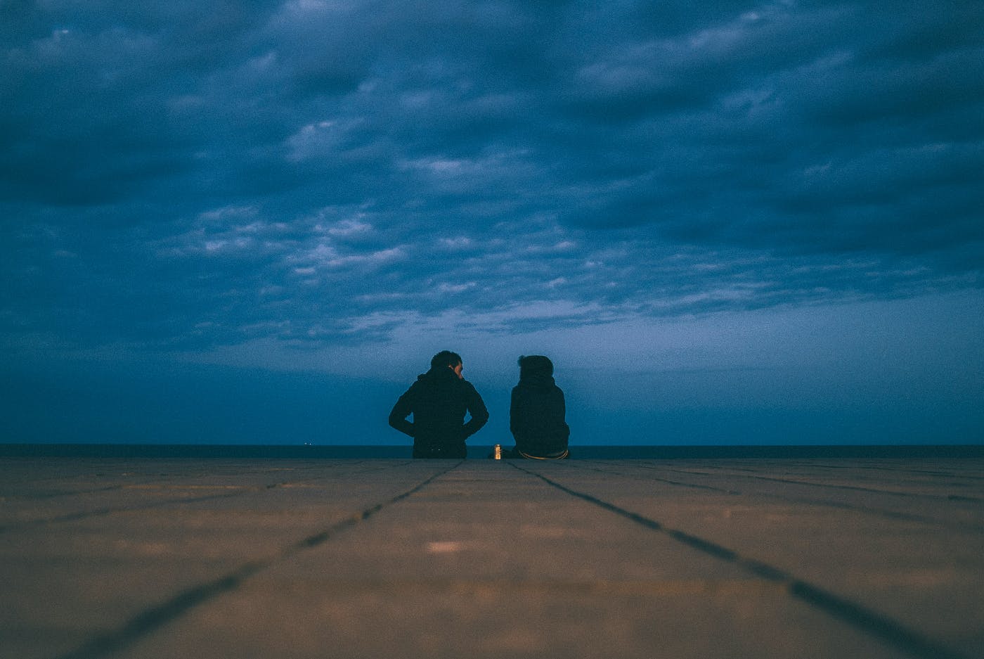 Two people sitting at the end of a pier talking