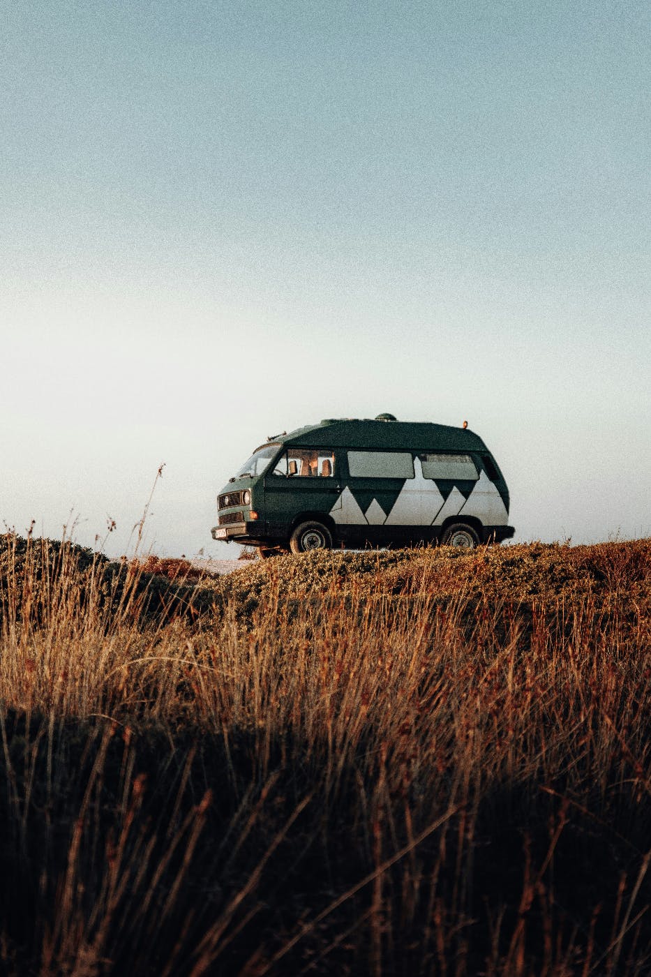 A black mini van with white mountains painted on it in a field