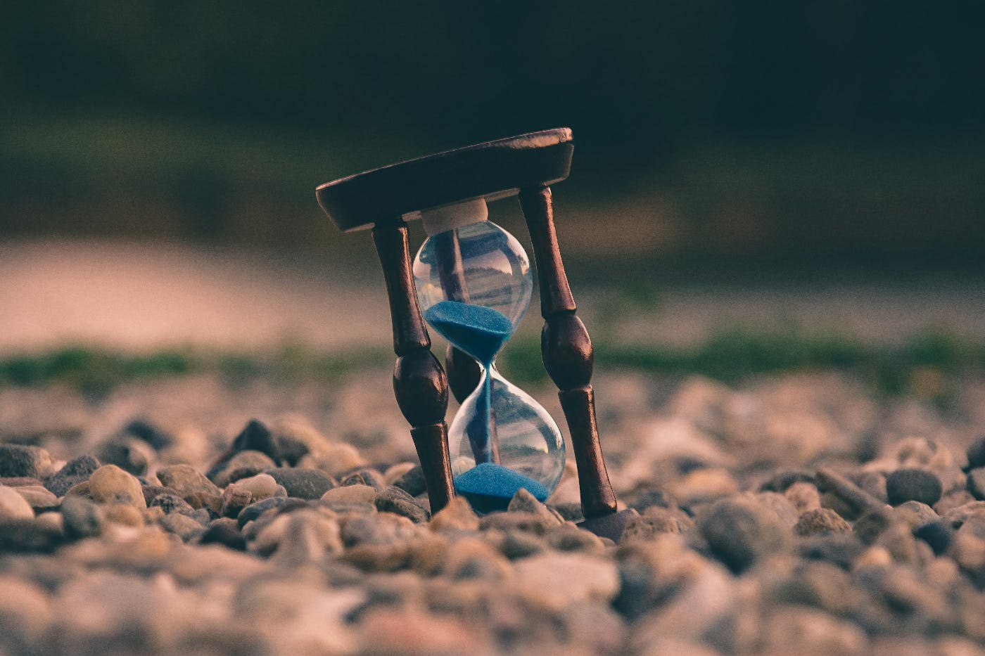 An hour glass with blue sand sitting on a rocky landscape