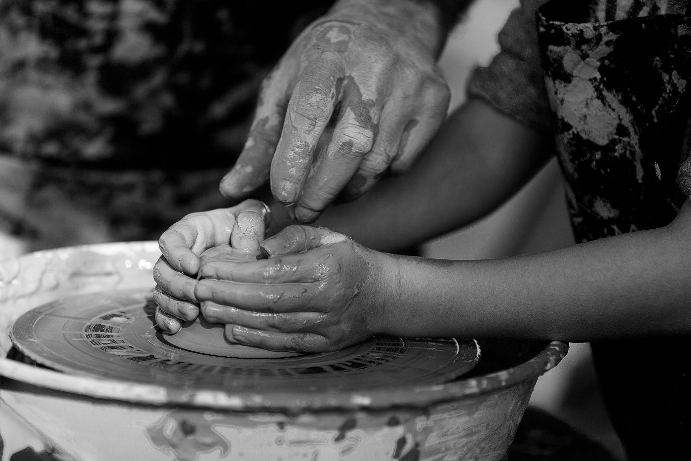 A child's hands working a potter's wheel with an adult hand guiding