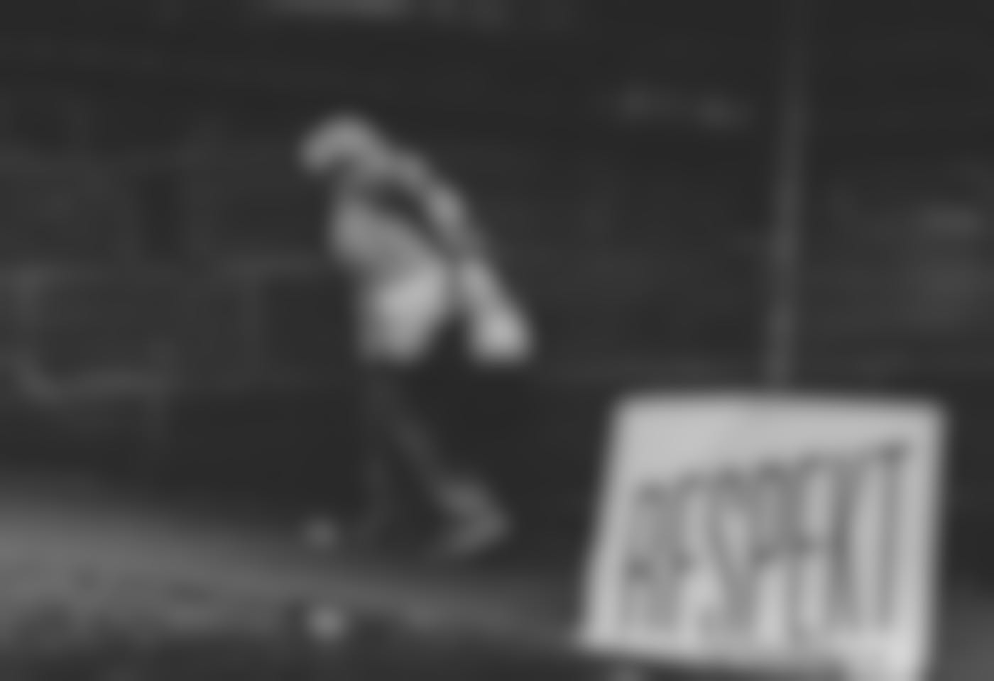 An older woman carrying groceries passes a sign falling off a pole reading RESPEKT