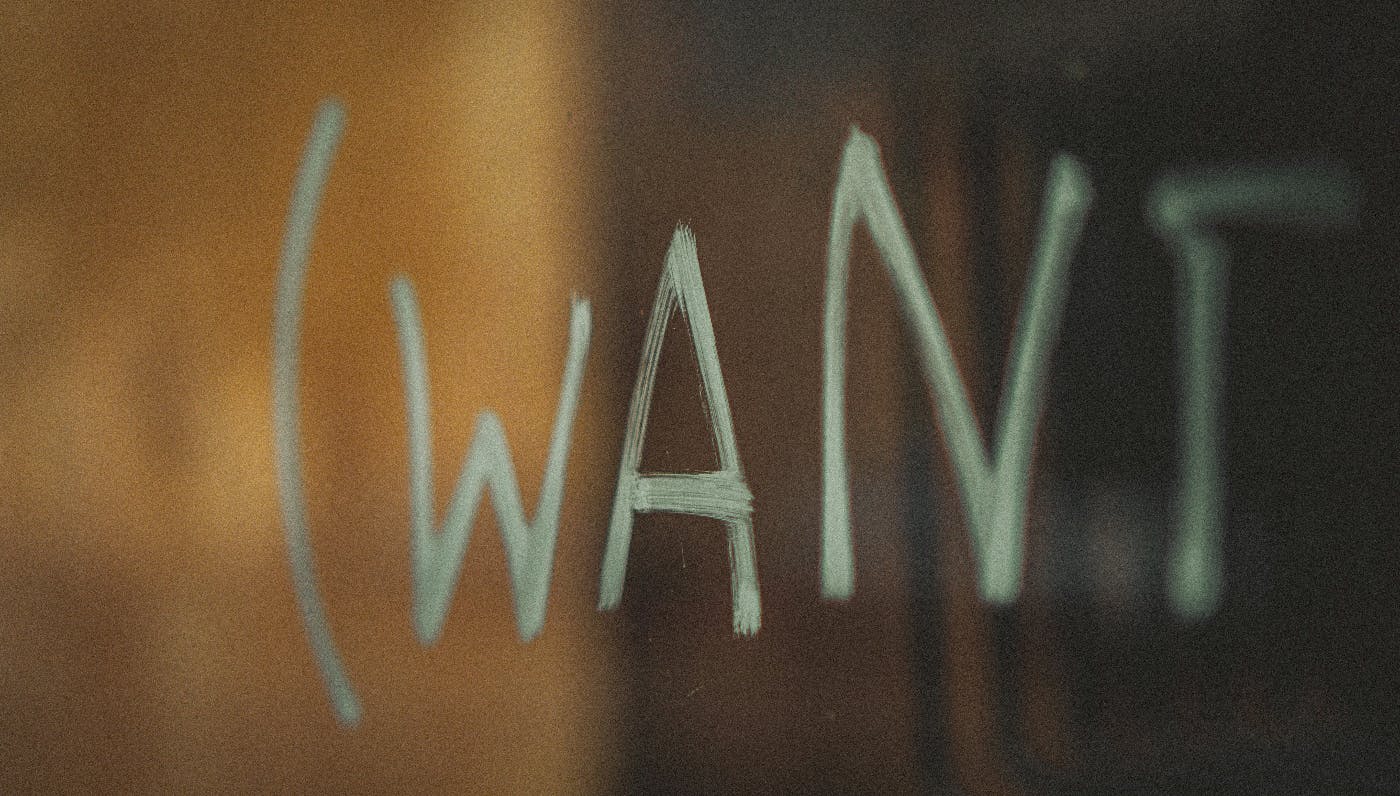 The word WANT written with gold sharpie on a glass panel