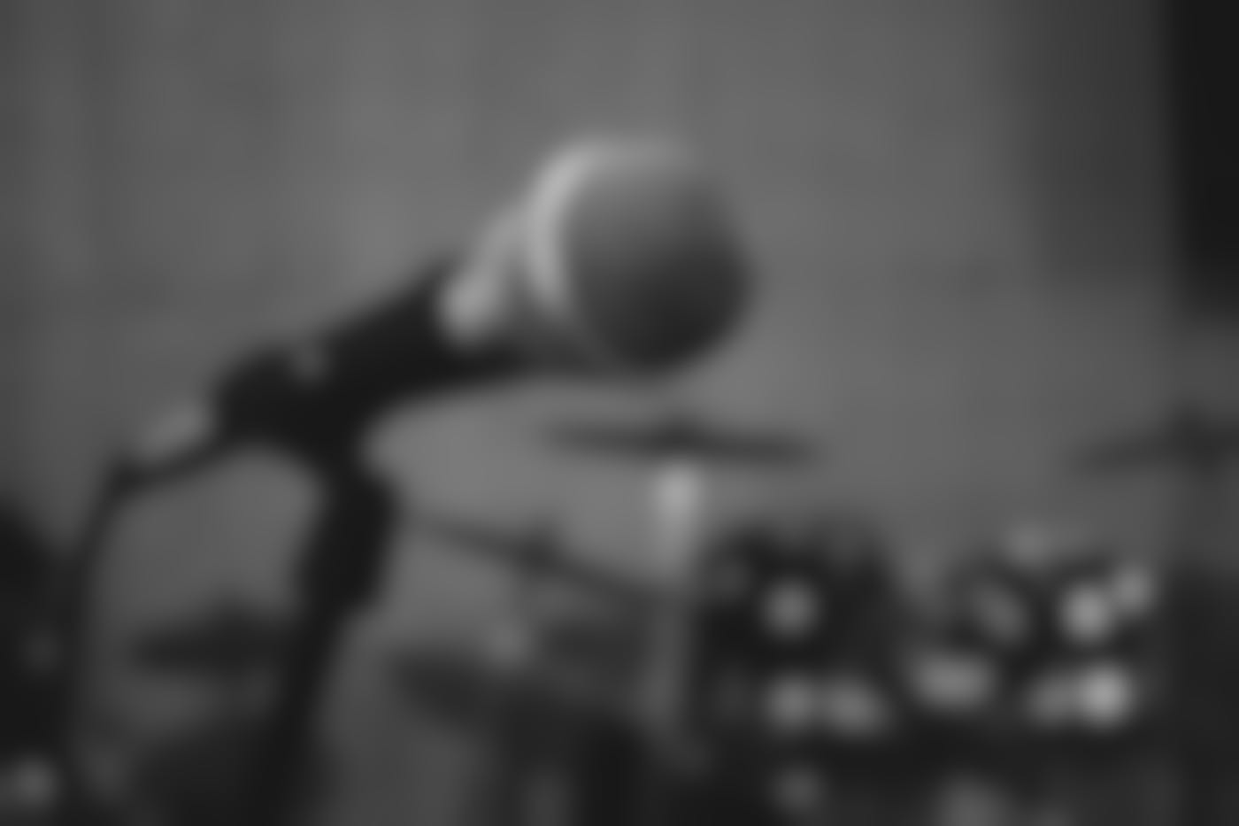 black and white shot of a mic on a stand with a drum kit in the background