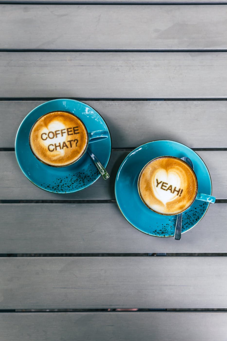 Two filed blue coffee cups with writing in the foam, left: coffee chat? Right: Yeah!