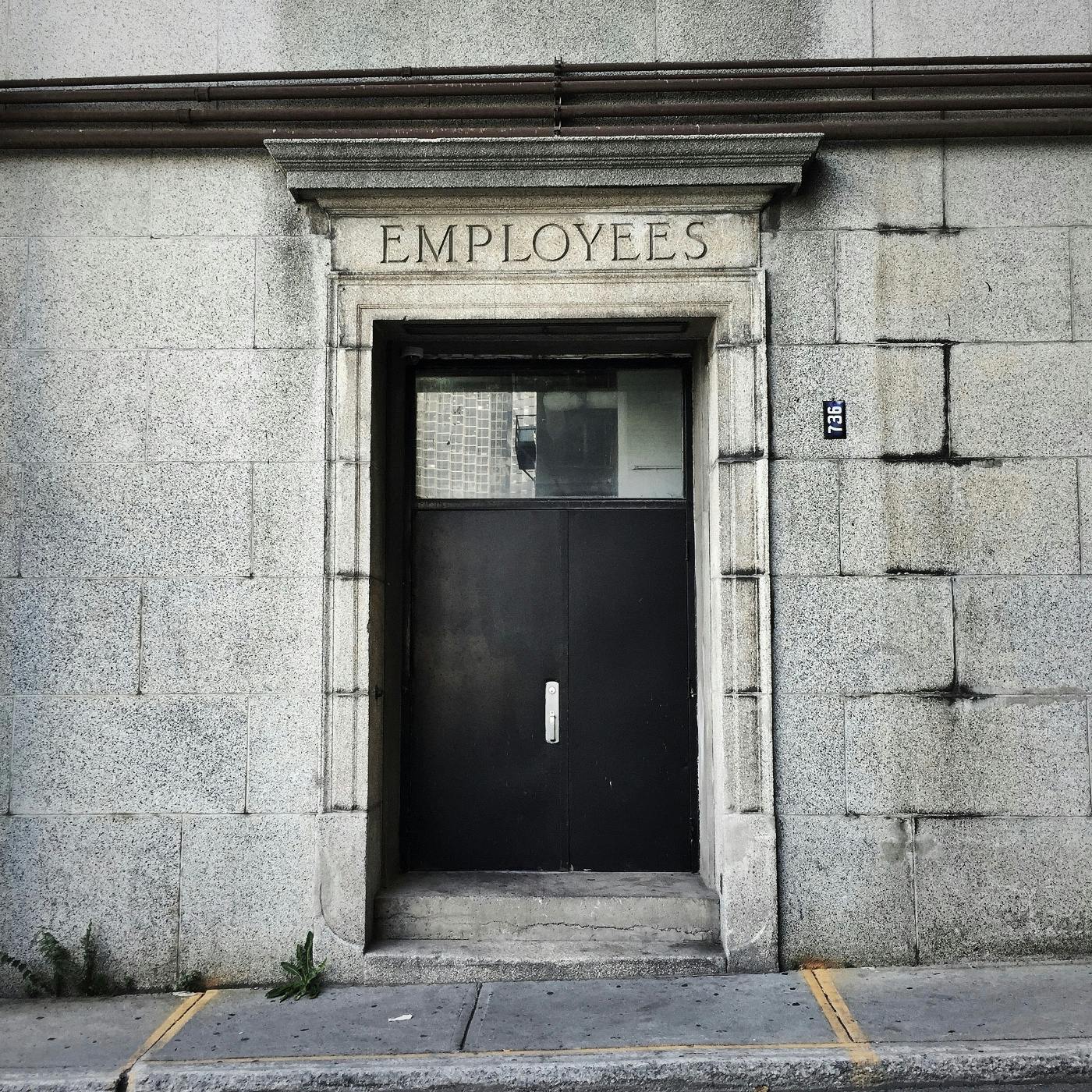 An austere concrete wall with a steel door and "employees" carved over the entrance