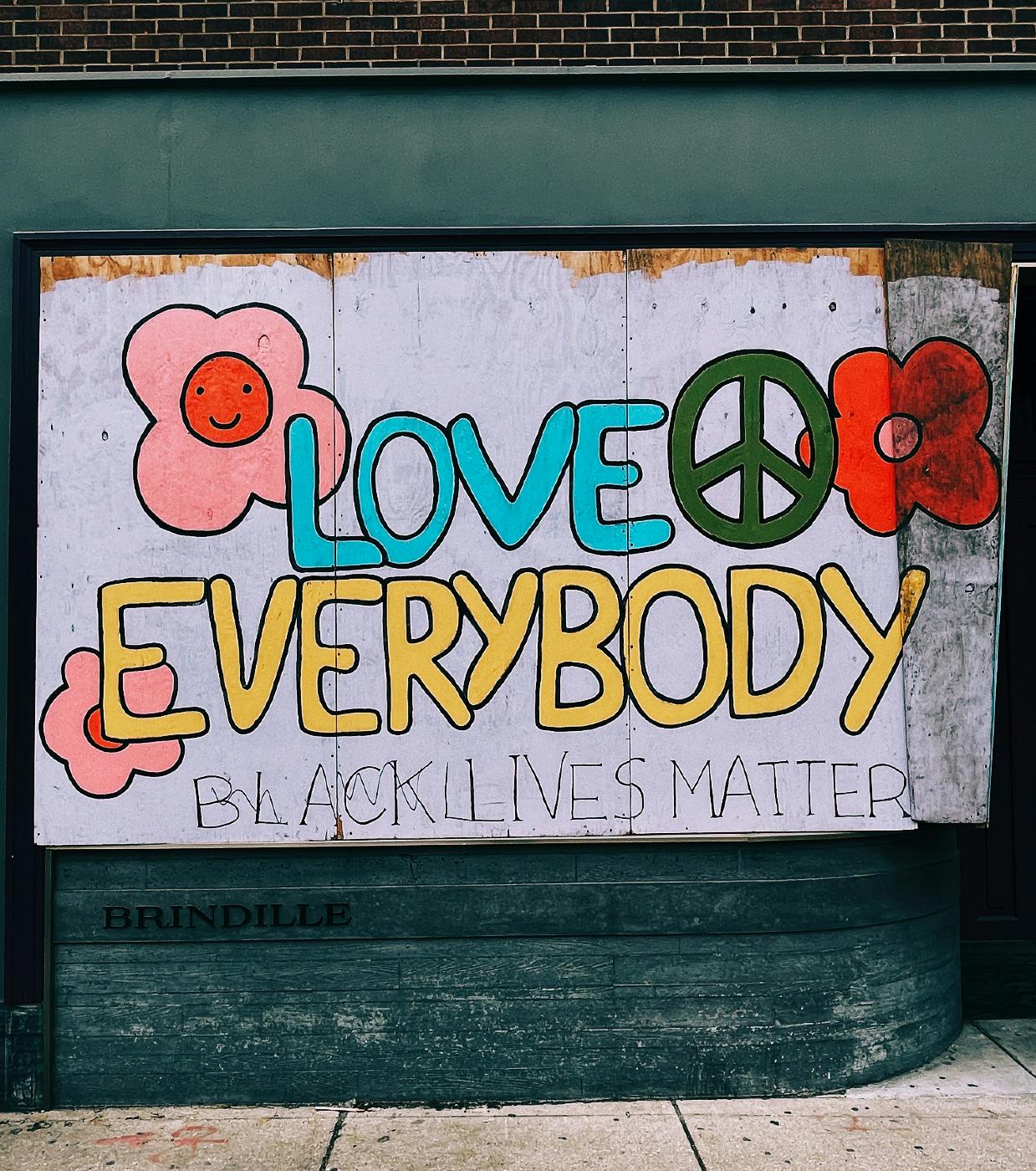 graffiti on a wall with flowers and a peace sign and the words: Love Everybody and Black Lives Matter