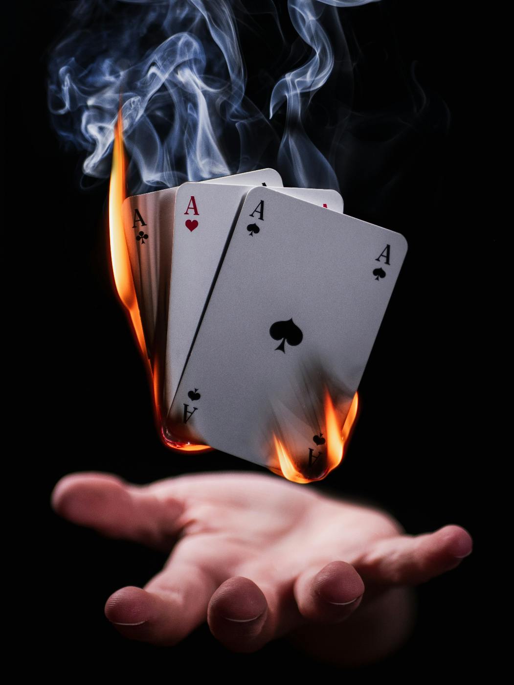 3 aces on fire hovering above a man's hand