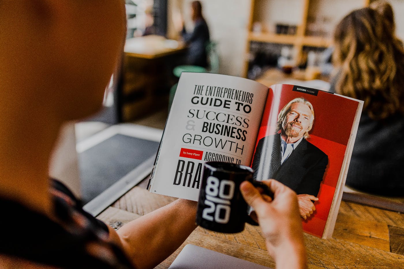 a kid holding a black 80\20 mug while looking at an article about Richard Branson