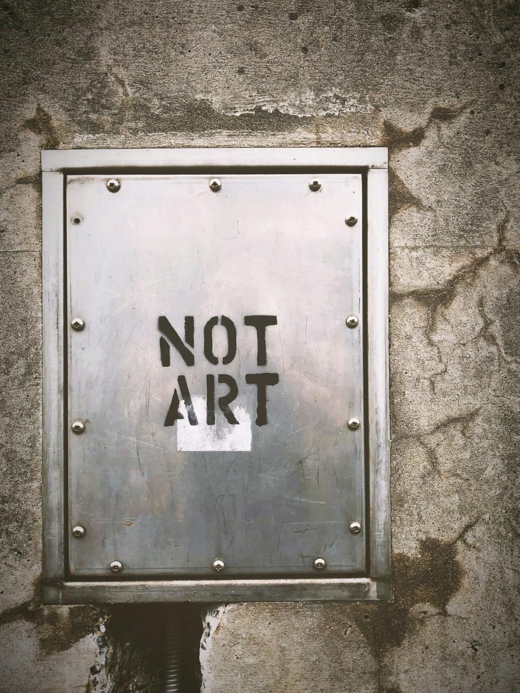 A steel panel in a stone wall with Not Art stenciled on it