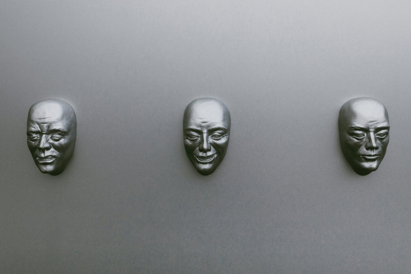 Three silver masks of the same man but in different emotional states