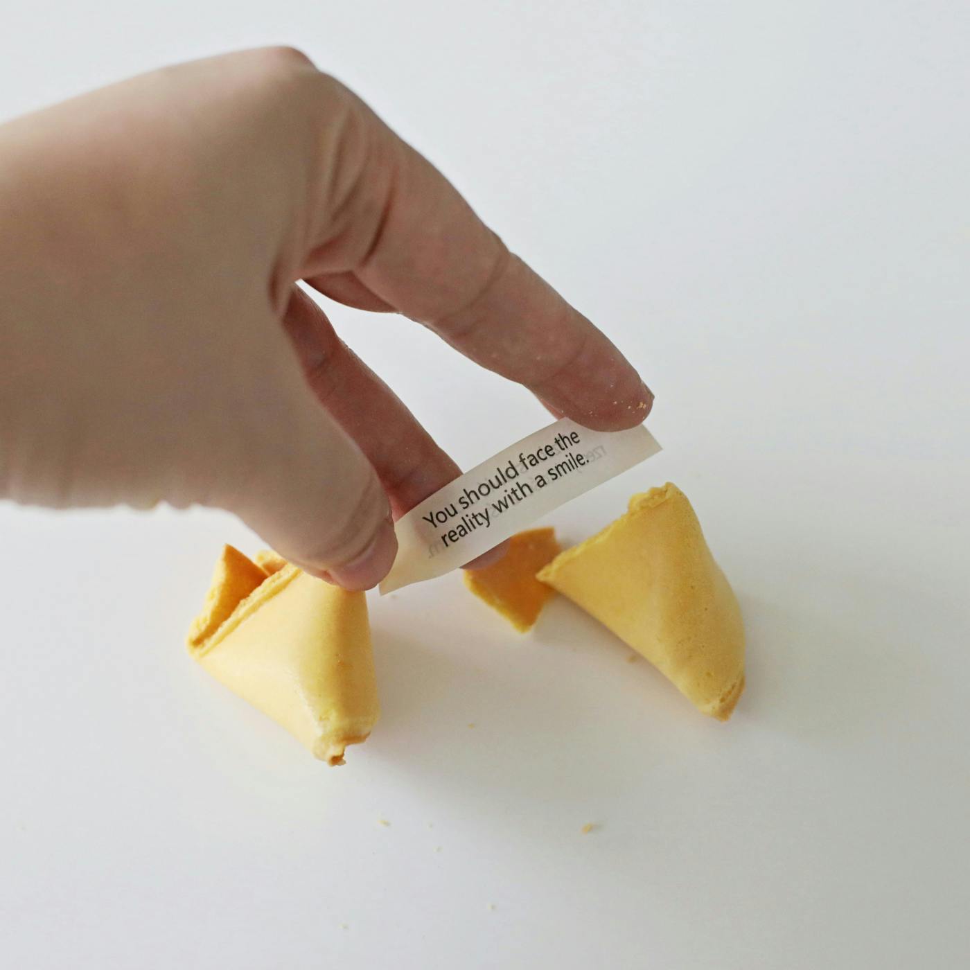 A broken fortune cookie and a hand holding the fortune that reads: You Should Face the Reality with a Smile