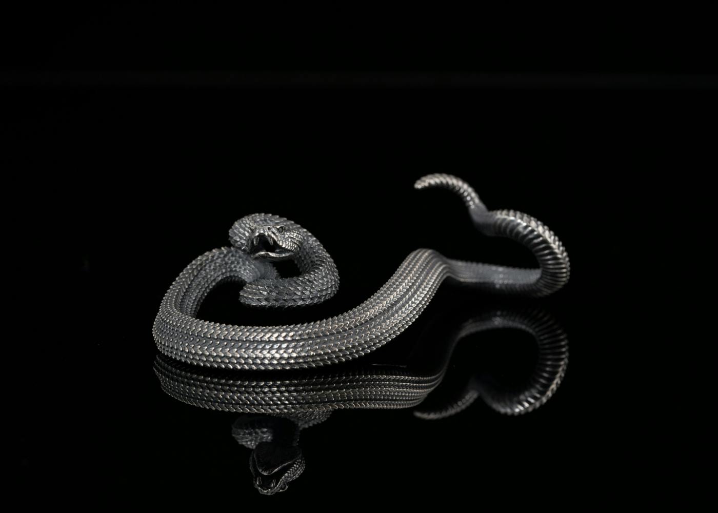 A silver statue of a rattle snake against a black background