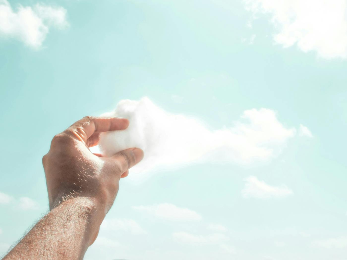 A person's hand seemingly pulling a piece of a cloud out of the sky